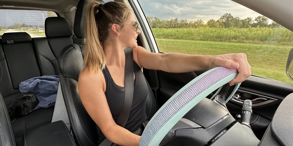 blonde girl driving with mint rhinestone steering wheel cover. countryside road background